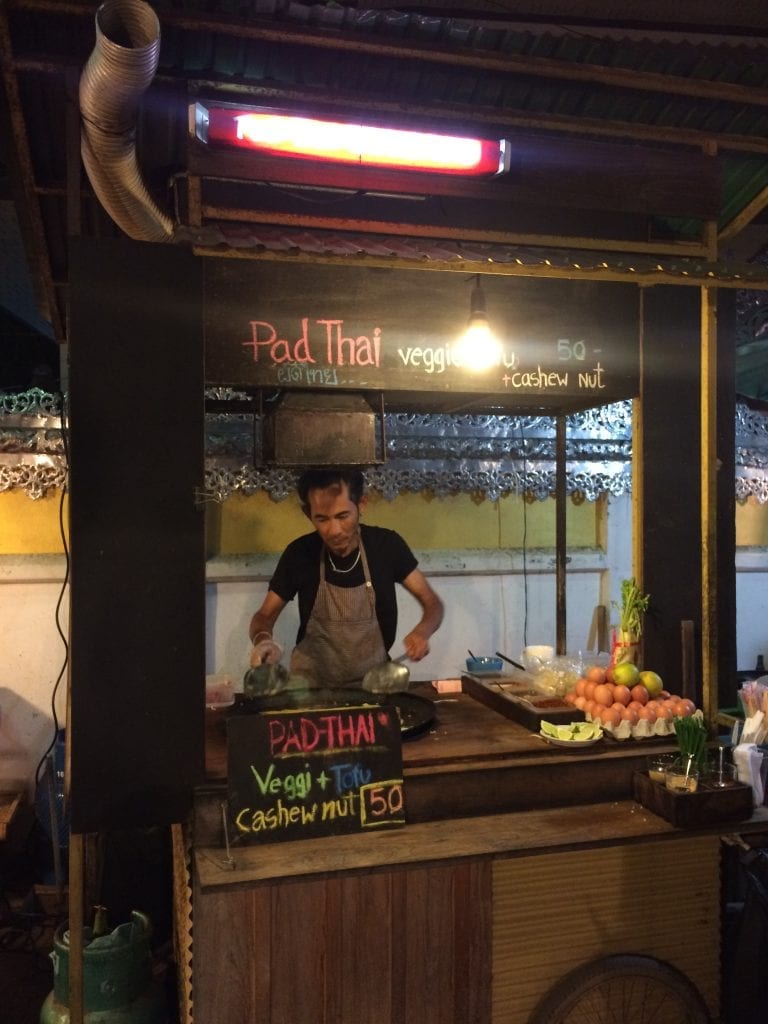 Eating stir fried street food from a local vendor cooking at his stall in Thailand. 