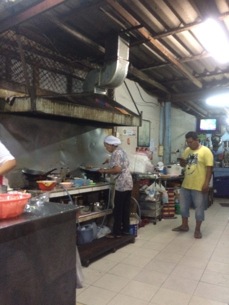 Roadside street food kitchen, showing a lady cooking at her stove in Thailand. 