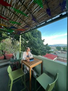 Female editor seated at a high table with an iPad, on a rooftop terrace.