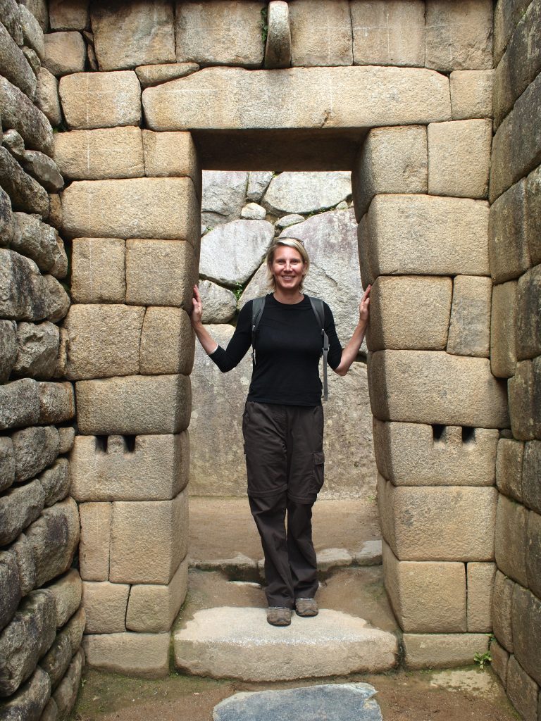 Blonde woman wearing a black top and brown trousers standing in the doorway of a building in Machu Picchu