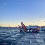 Parked airplanes on the airport tarmac through a plane window with raindrops on it