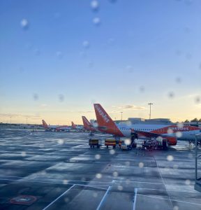 Parked airplanes on the airport tarmac through a plane window with raindrops on it