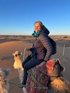 Woman wearing winter layers sitting on a white camel in the desert